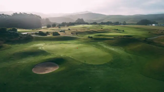 Aerial view of a bunkered green toward the coastal hills