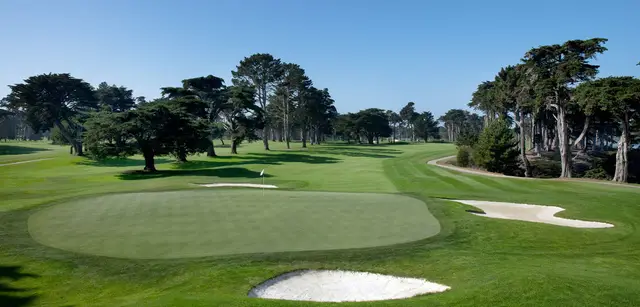 Green guarded by bunkers, framed by cypress trees
