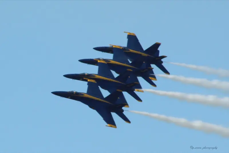 Four Blue Angels F/A-18 jets in tight diamond formation trailing white smoke against a clear blue sky